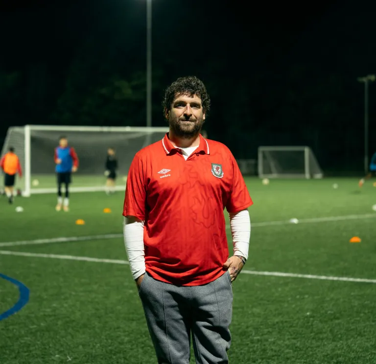Club founder Delwyn Derrick standing on a football pitch while a game takes places behind him